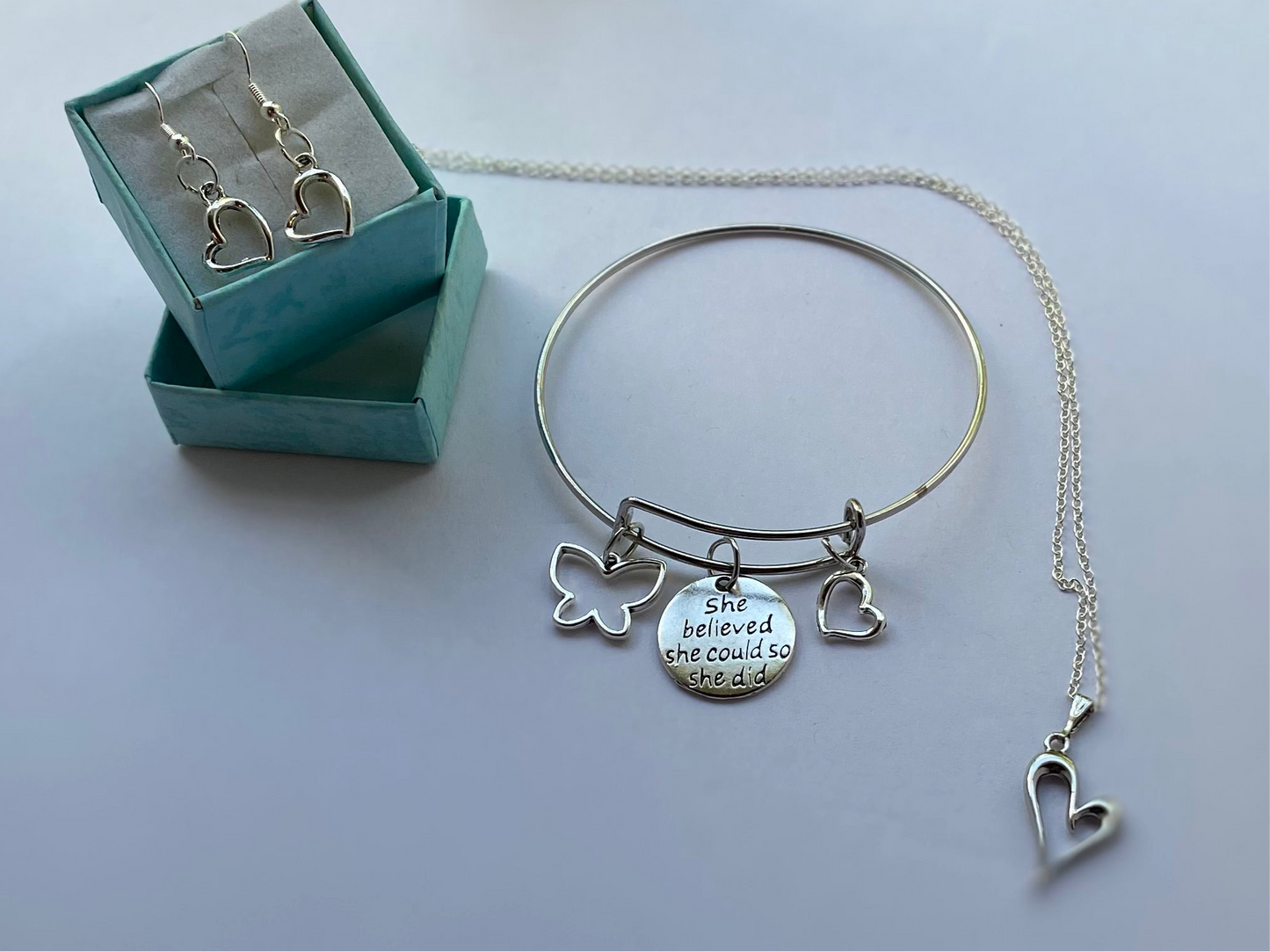 Silver necklace, earrings, and bangle set with heart, butterfly charms, and inspirational "she believed she could so she did" message.