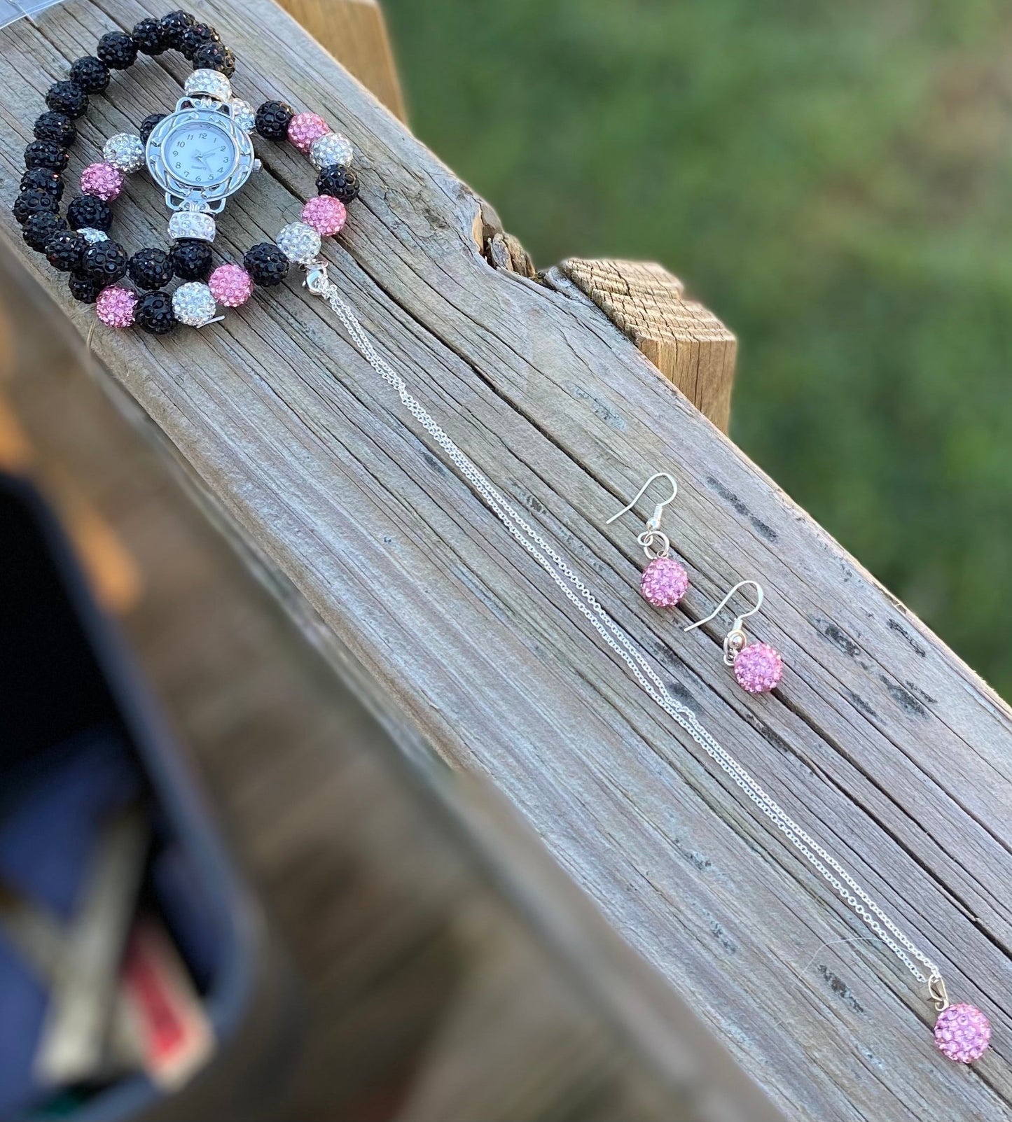 Watch bracelet necklace and earrings set with black and pink beaded design on wooden surface