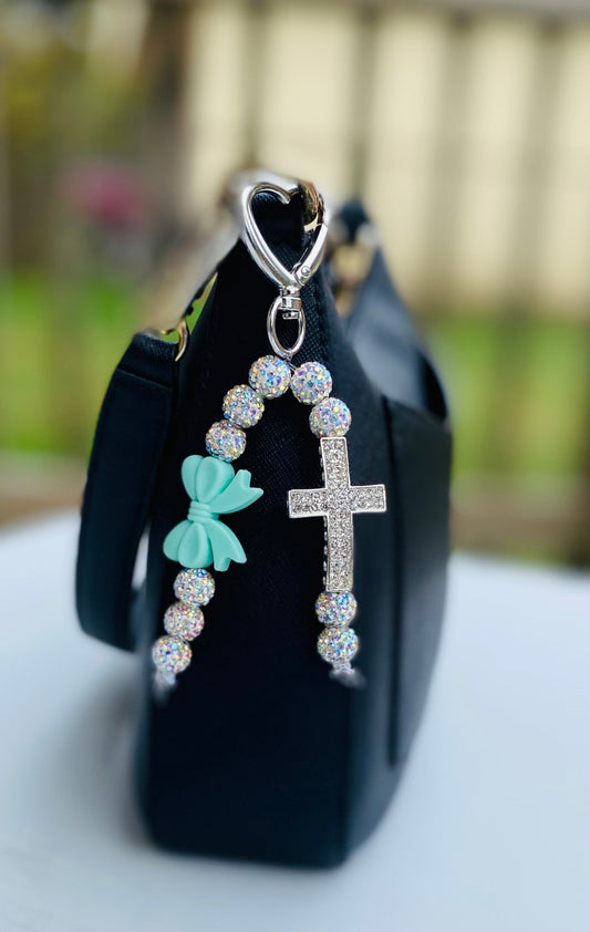 Sparkling bag charm with rhinestone beads, a cross, and a turquoise bow keychain attached to a black purse