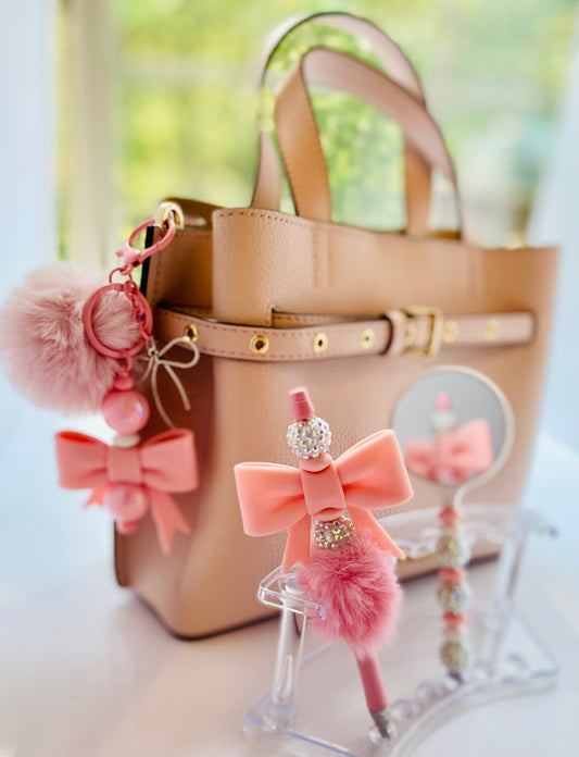 Pink bag charm, pen, and mirror set with bows, pom poms, and shiny beads.